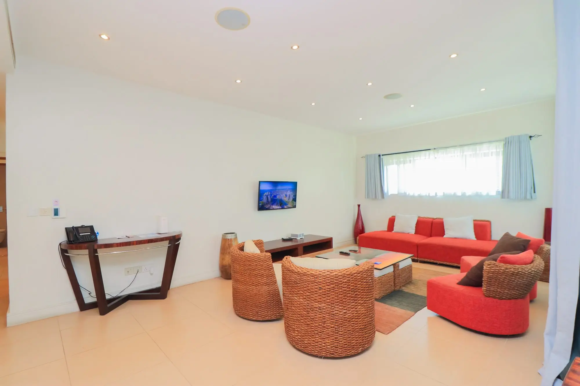 Lounge with red sofa, wicker armchairs and smart TV at Nyali Marina Stays apartment, Mombasa
